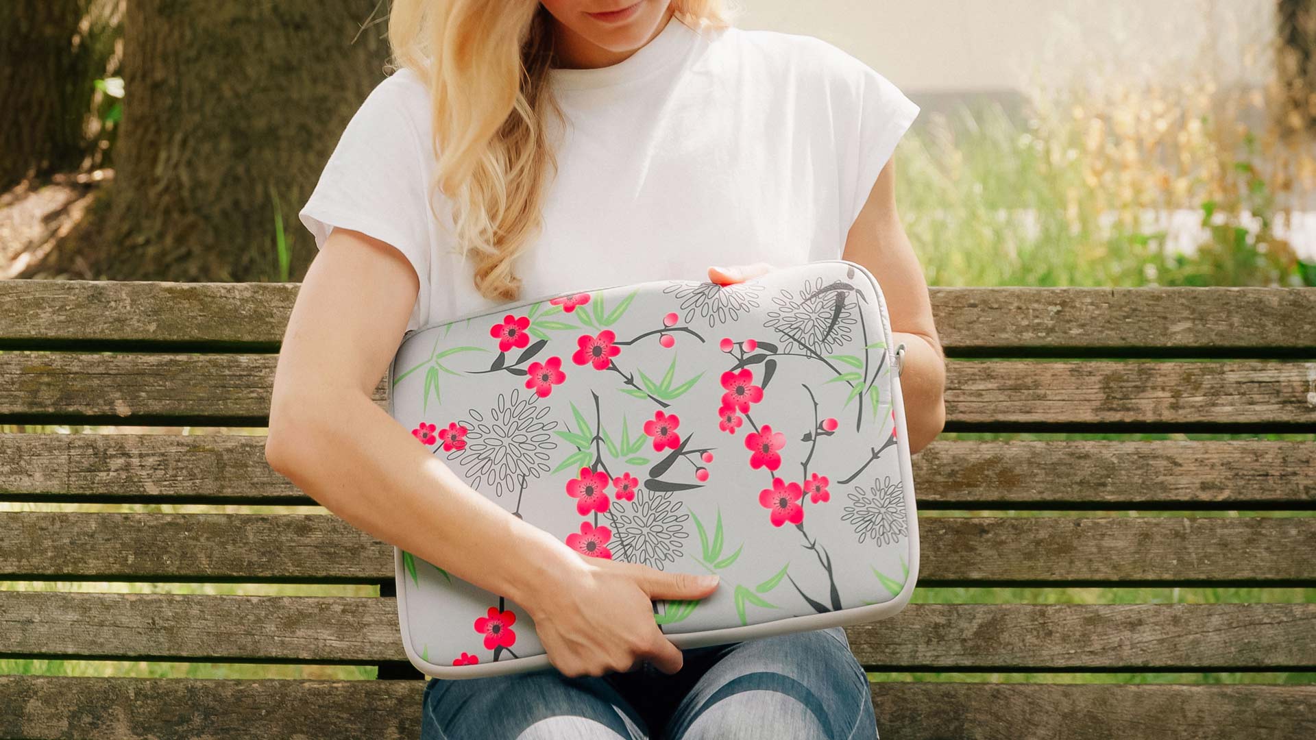 Banner: Frau sitzt bei sommerlichem Wetter auf einer Bank und hält LS104 Sakura Laptop-Schutzhülle in den Händen.